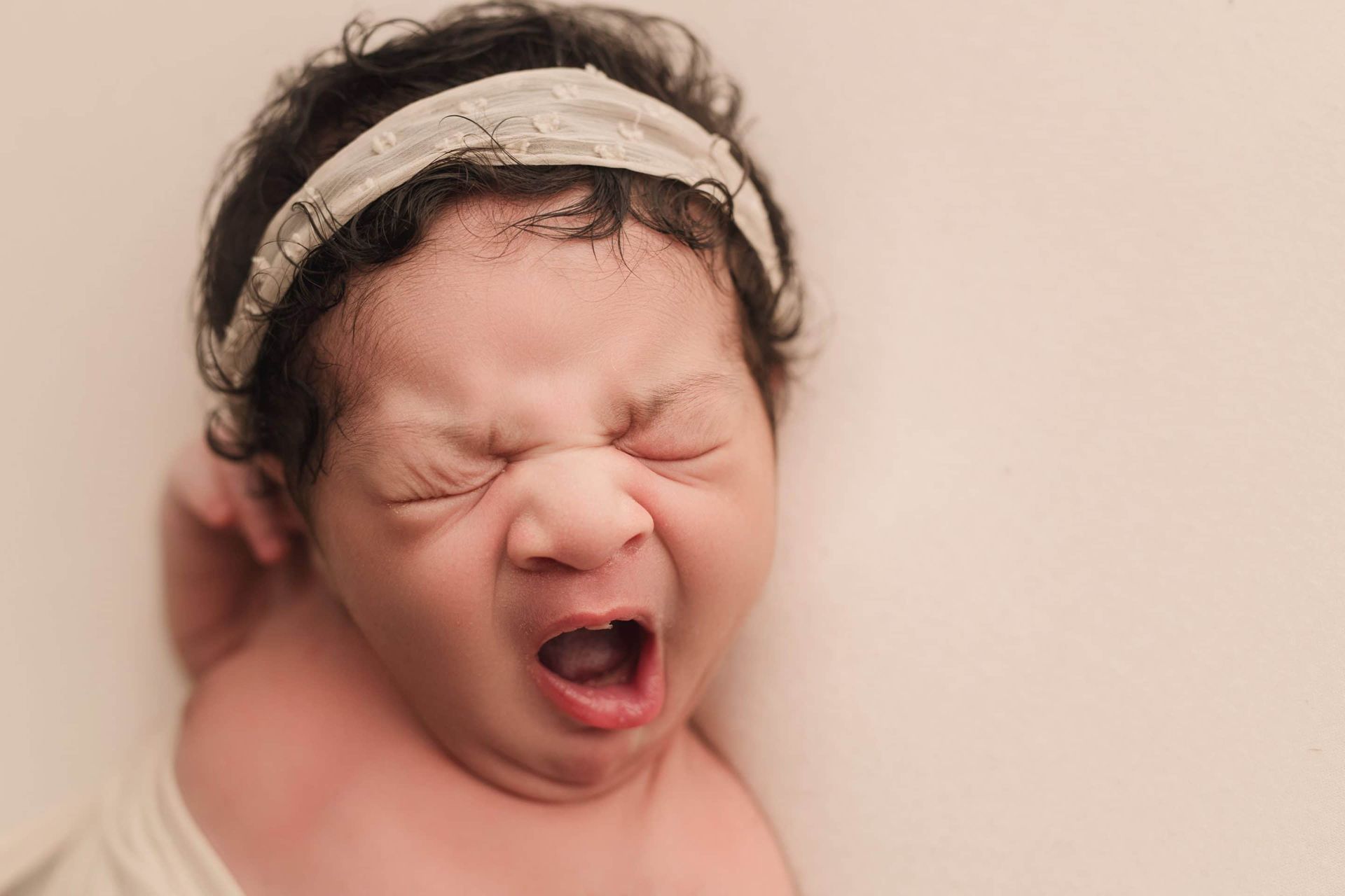 A newborn baby girl is crying with her mouth open.