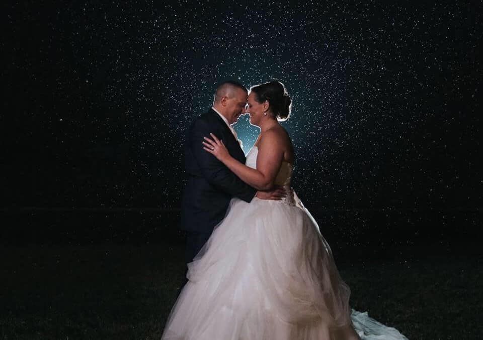 A bride and groom are dancing under a starry night sky.