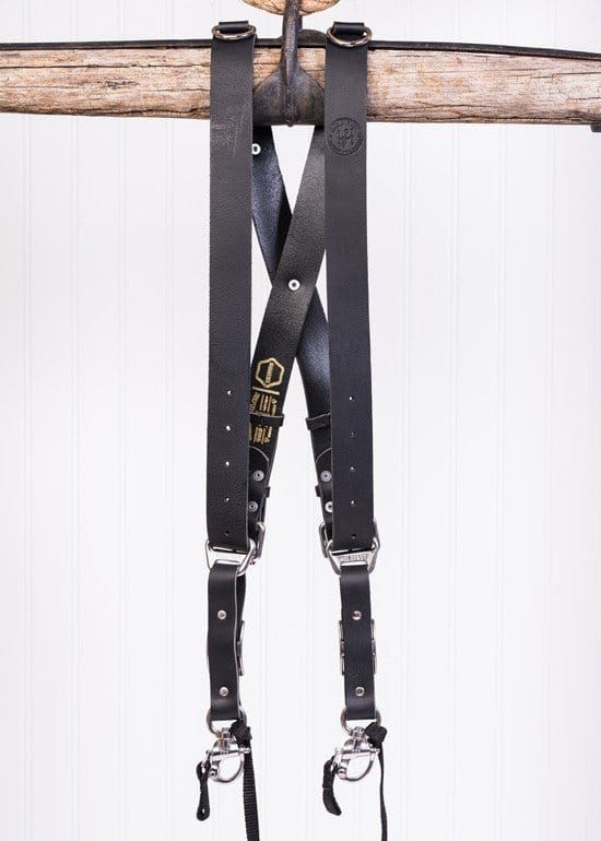 A pair of black leather suspenders hanging from a piece of wood.