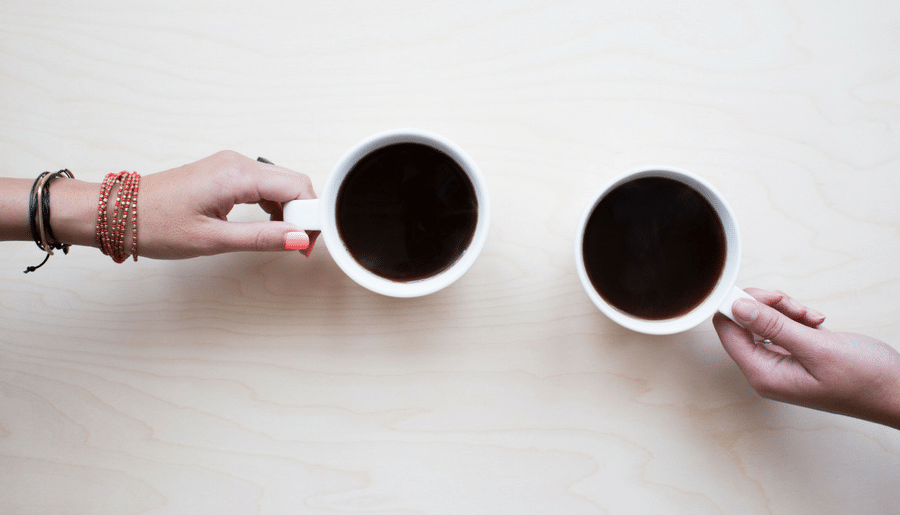 Two people are holding cups of coffee on a table.