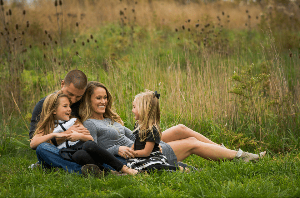 A family is sitting on a blanket in the grass.