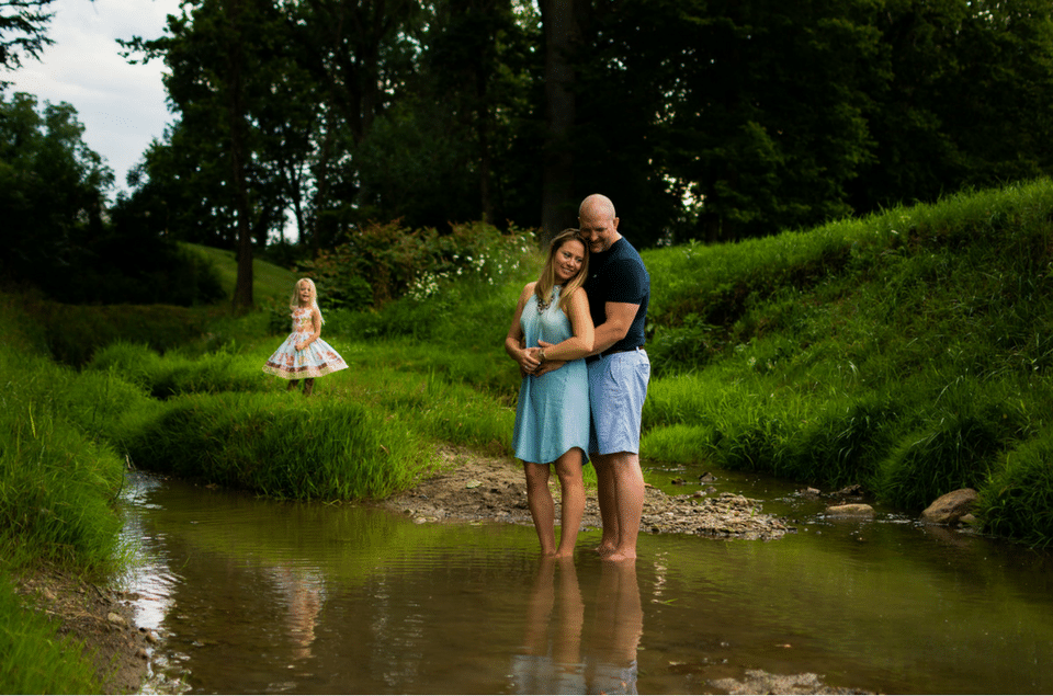 A man and woman are standing in a stream with a little girl in the background.