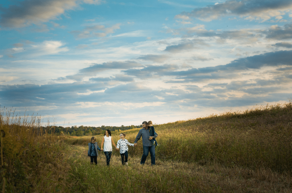 A family is walking through a field holding hands.