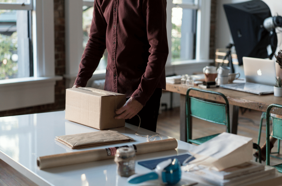 A man is standing next to a table holding a cardboard box.