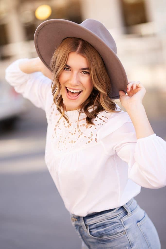 A woman wearing a hat and a white shirt is smiling.