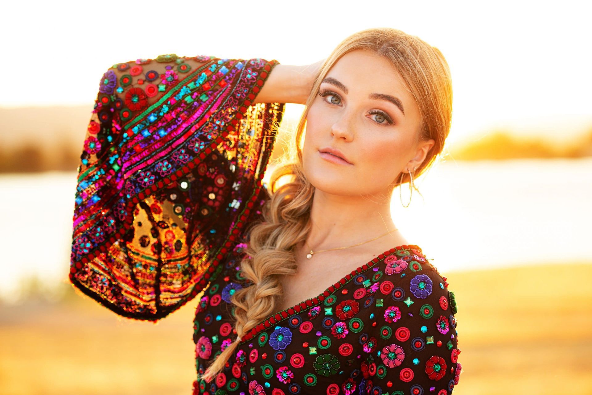 A woman in a colorful dress is standing in front of a body of water.