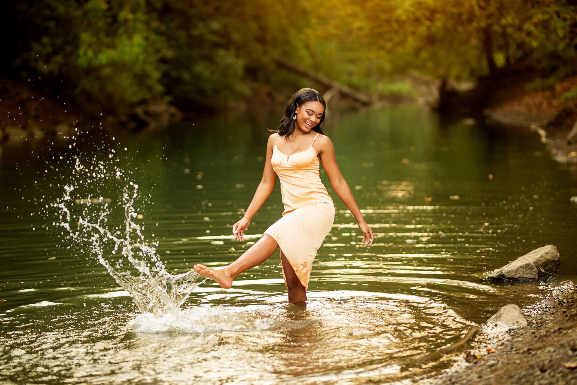 A woman in a dress is standing in a river with her foot in the water.