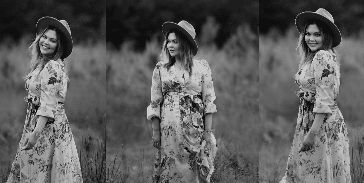 A woman in a floral dress and hat is standing in a field.