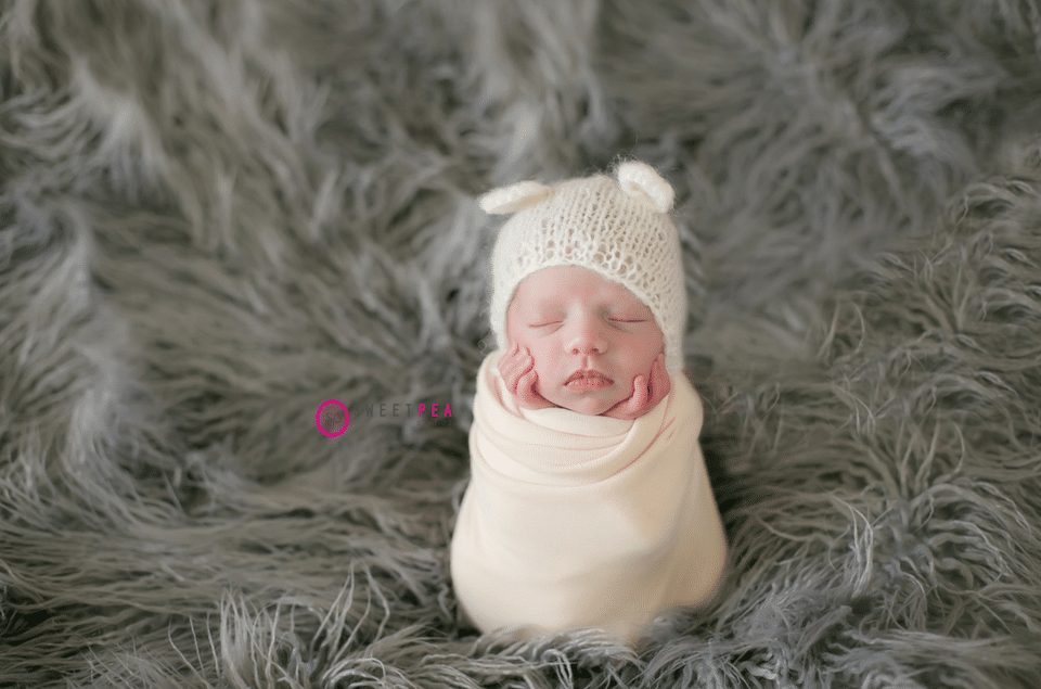 A newborn baby is wrapped in a white blanket and wearing a white hat.