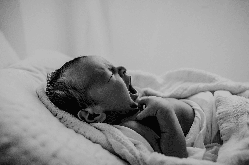 A black and white photo of a newborn baby laying on a bed.