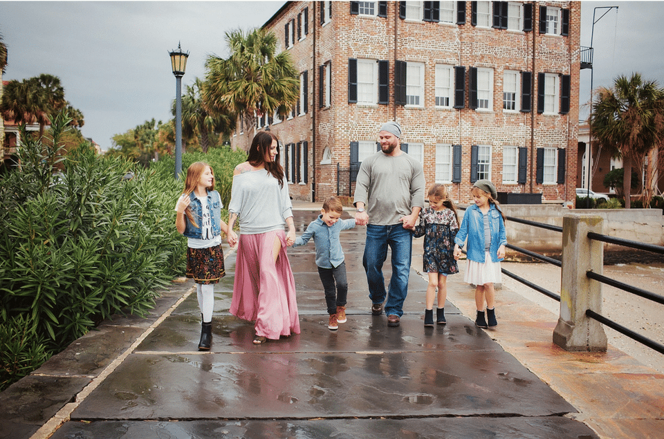 A family is walking across a bridge in the rain holding hands.