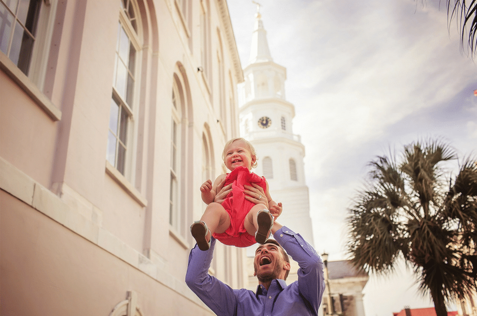 A man is holding a baby in his arms in front of a building.