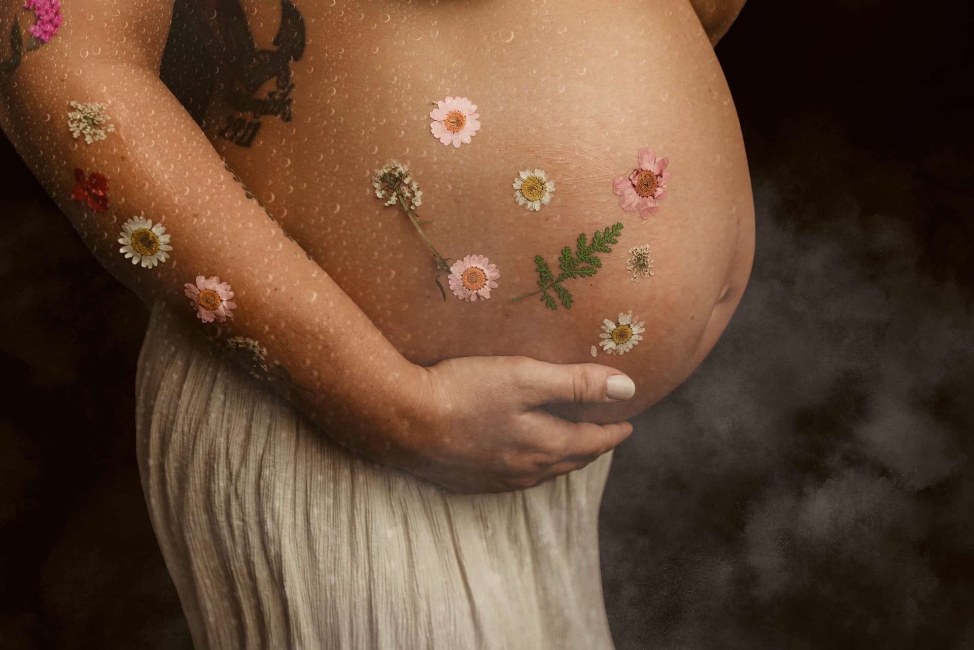 A pregnant woman with flowers on her belly is holding her belly.