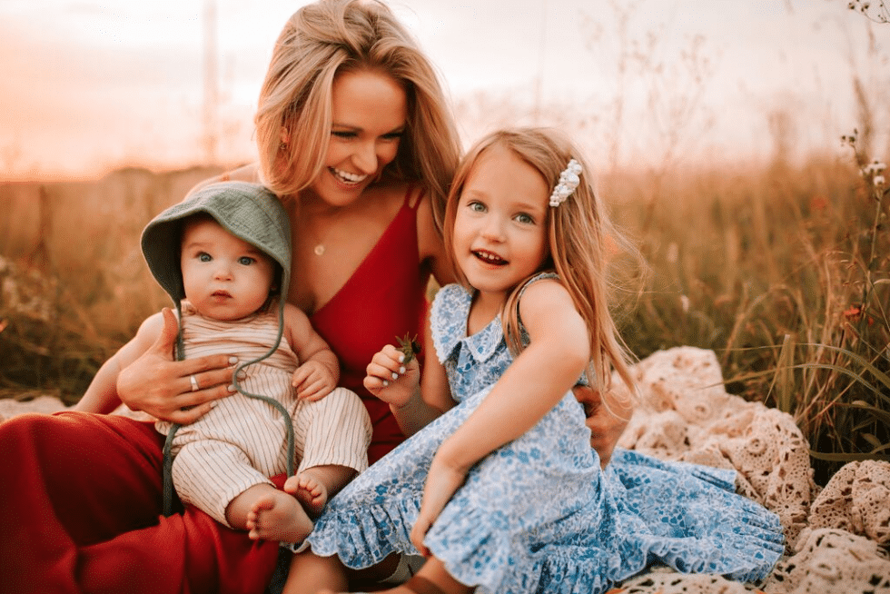 A woman is sitting in a field with two children.