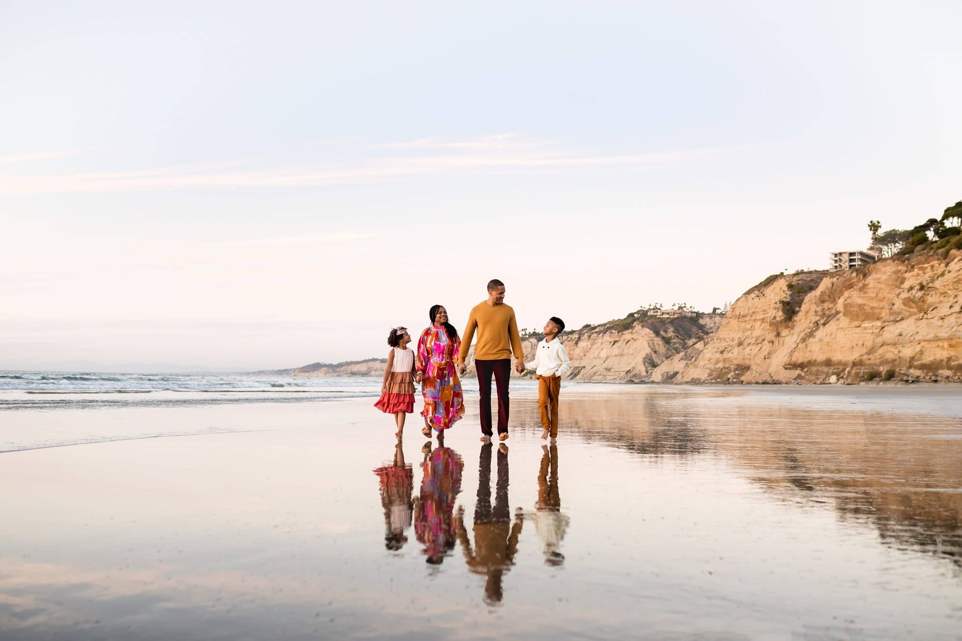 A family is walking along the beach holding hands.