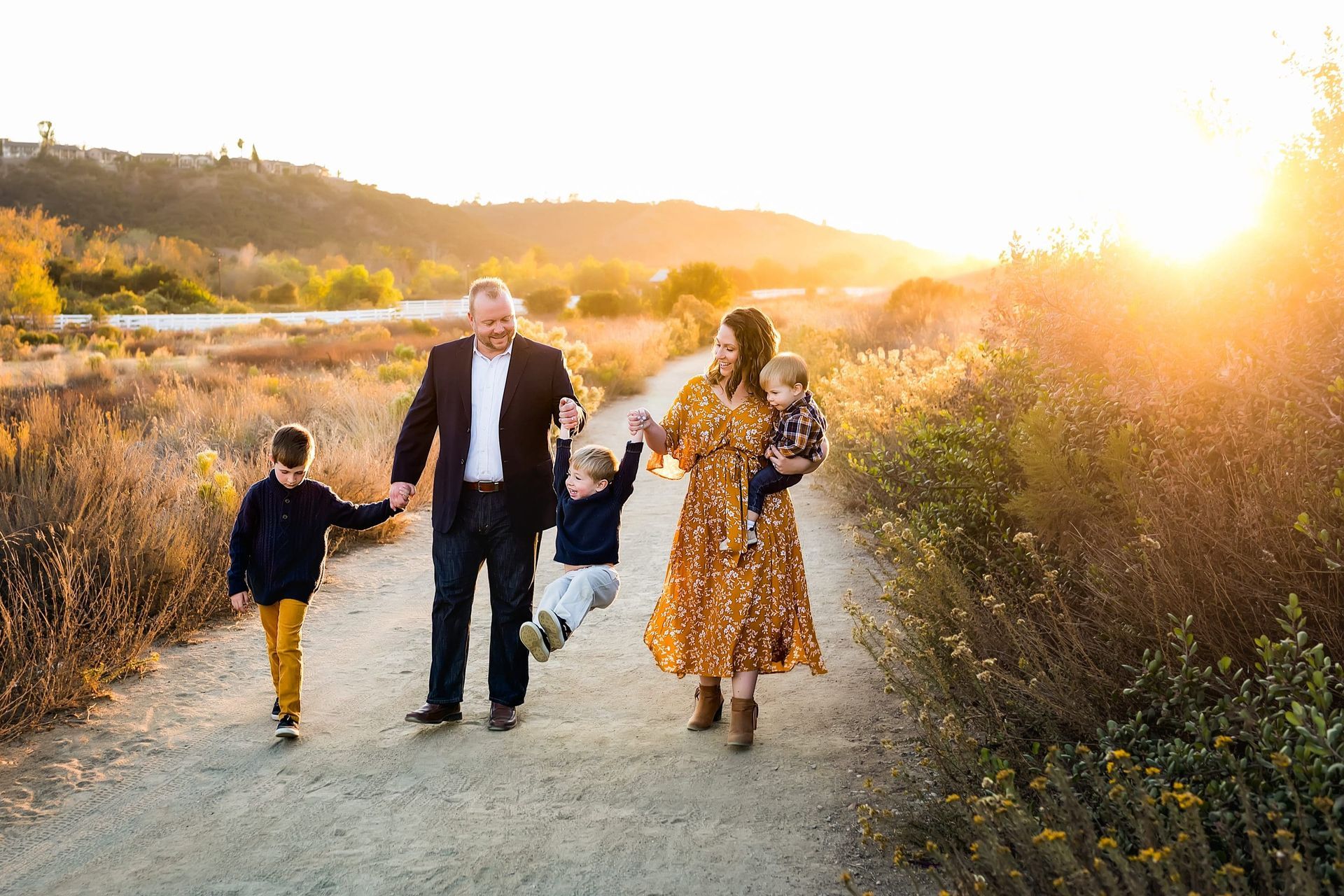 A family is walking down a dirt path holding hands at sunset.