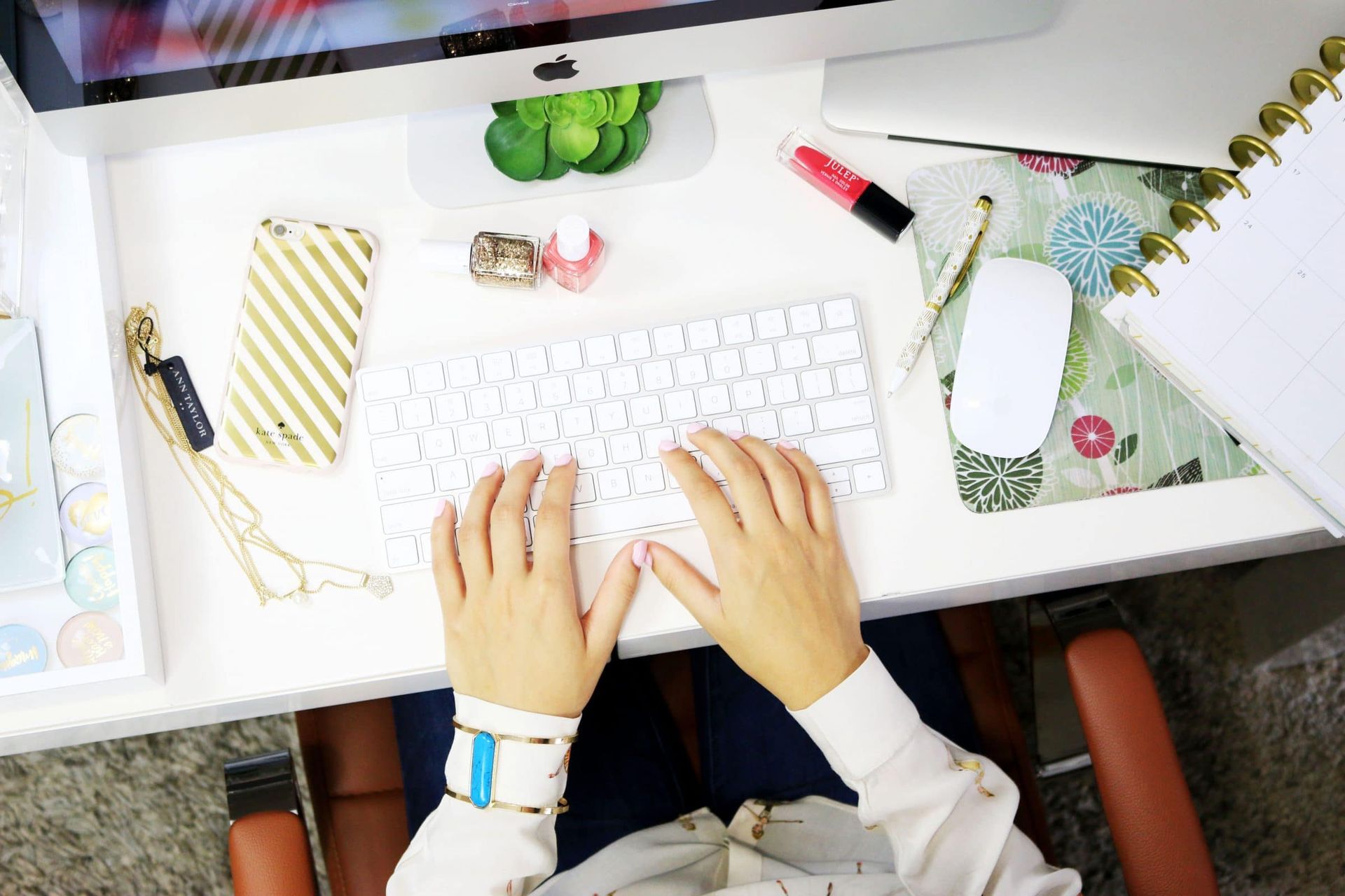 A woman is typing on a computer keyboard while sitting at a desk.