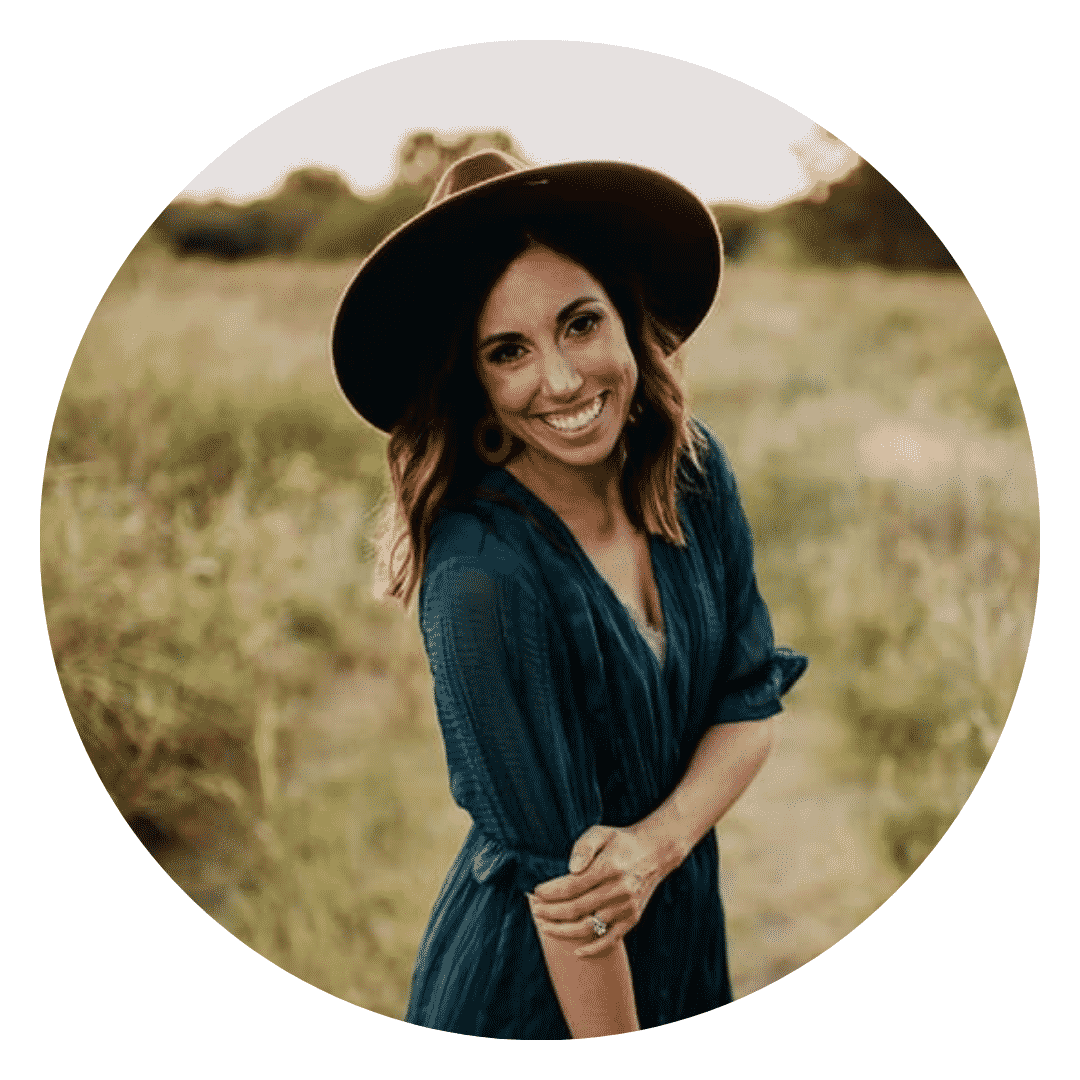 A woman wearing a hat and a blue dress is smiling in a field.