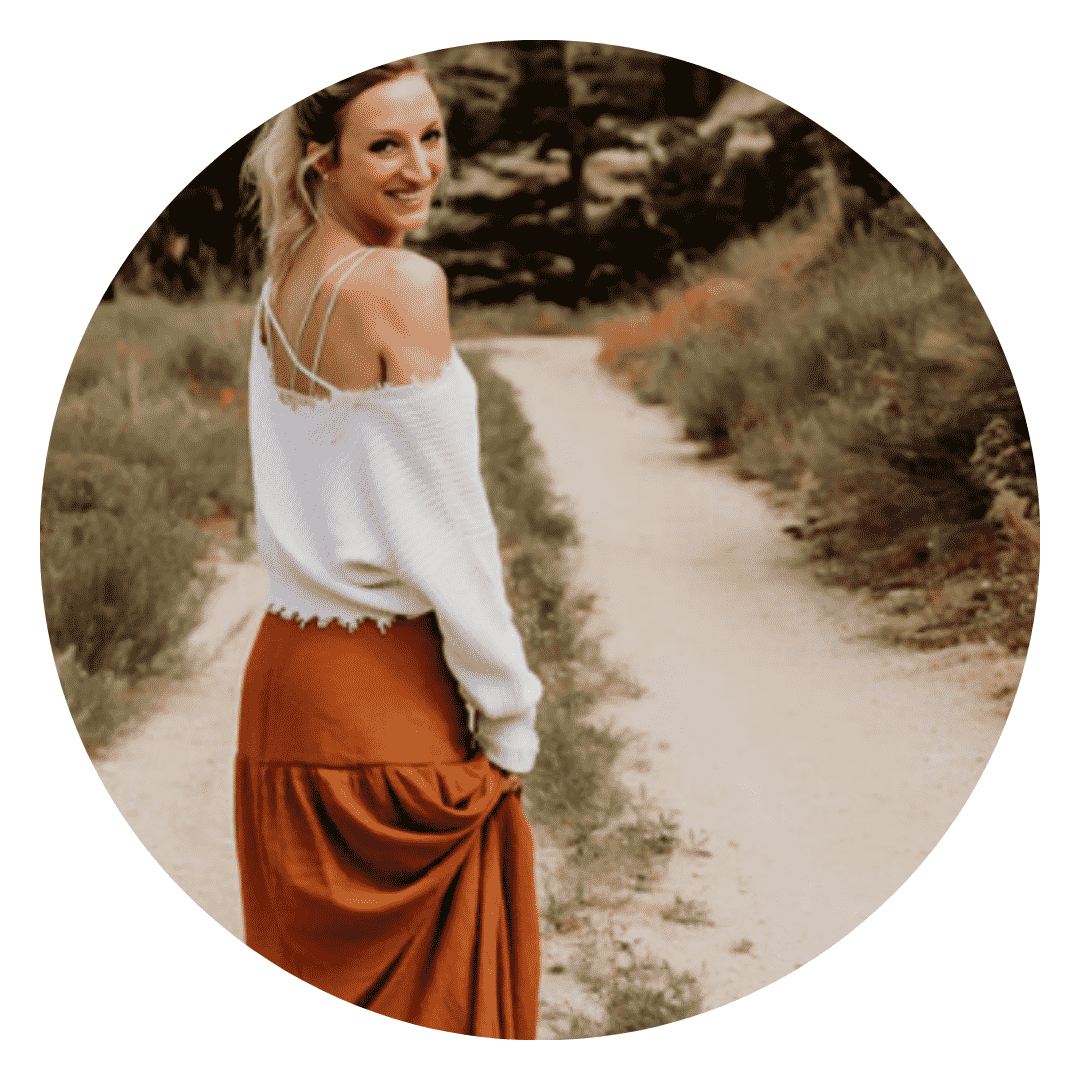 A woman in a white sweater and an orange skirt is standing on a dirt road.