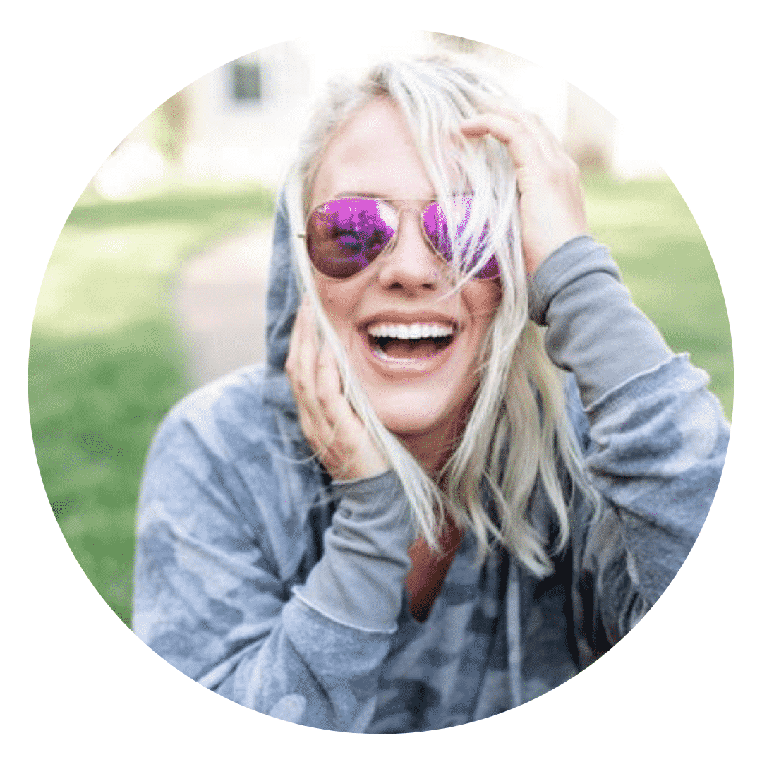 A woman wearing sunglasses and a hoodie is laughing.