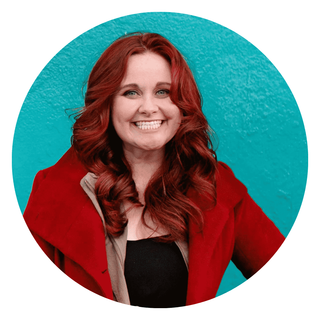 A woman with red hair is smiling in front of a blue wall.