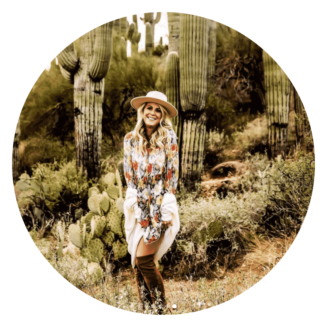 A woman is standing in front of a cactus in the desert.