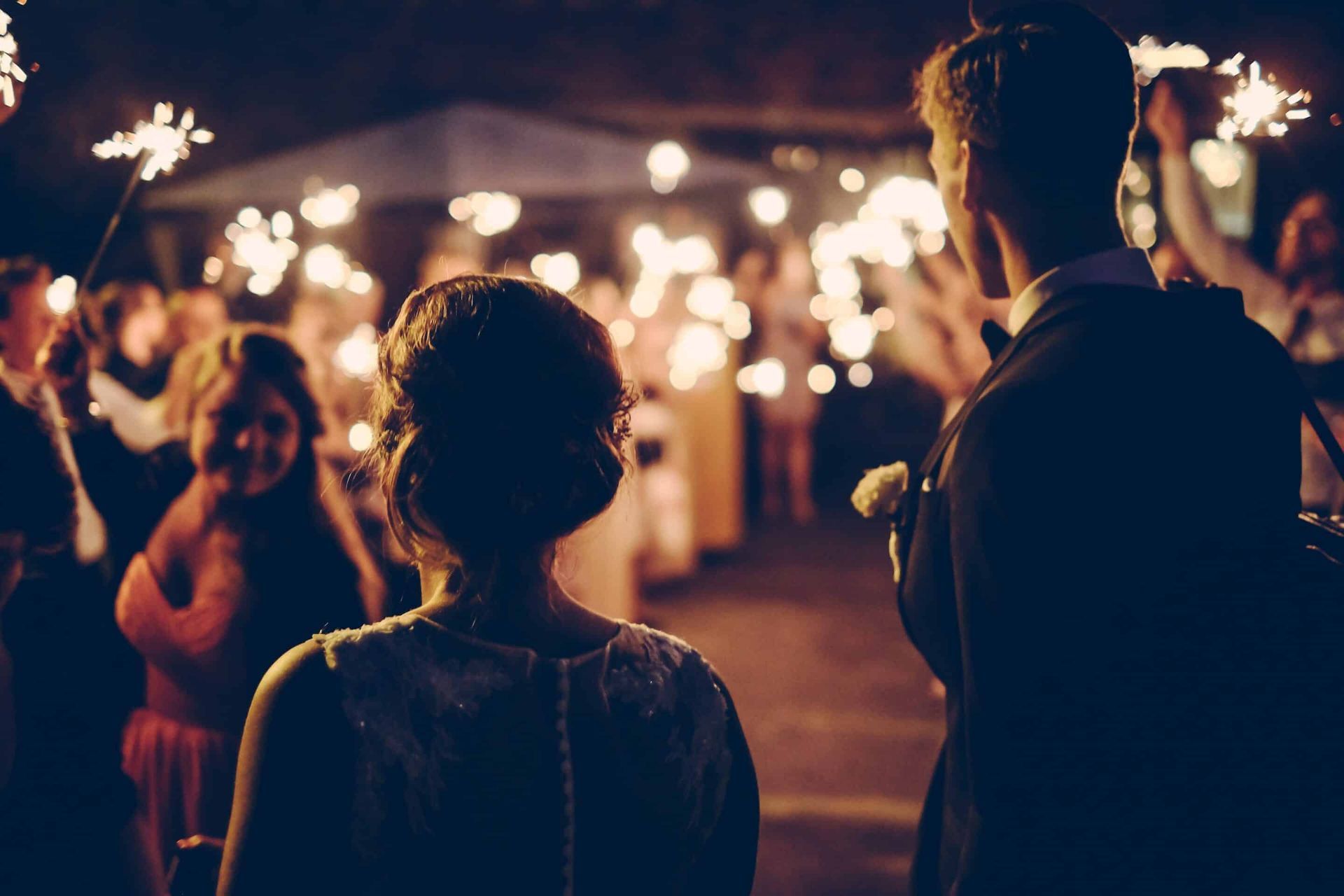 A bride and groom are holding sparklers at a wedding reception.