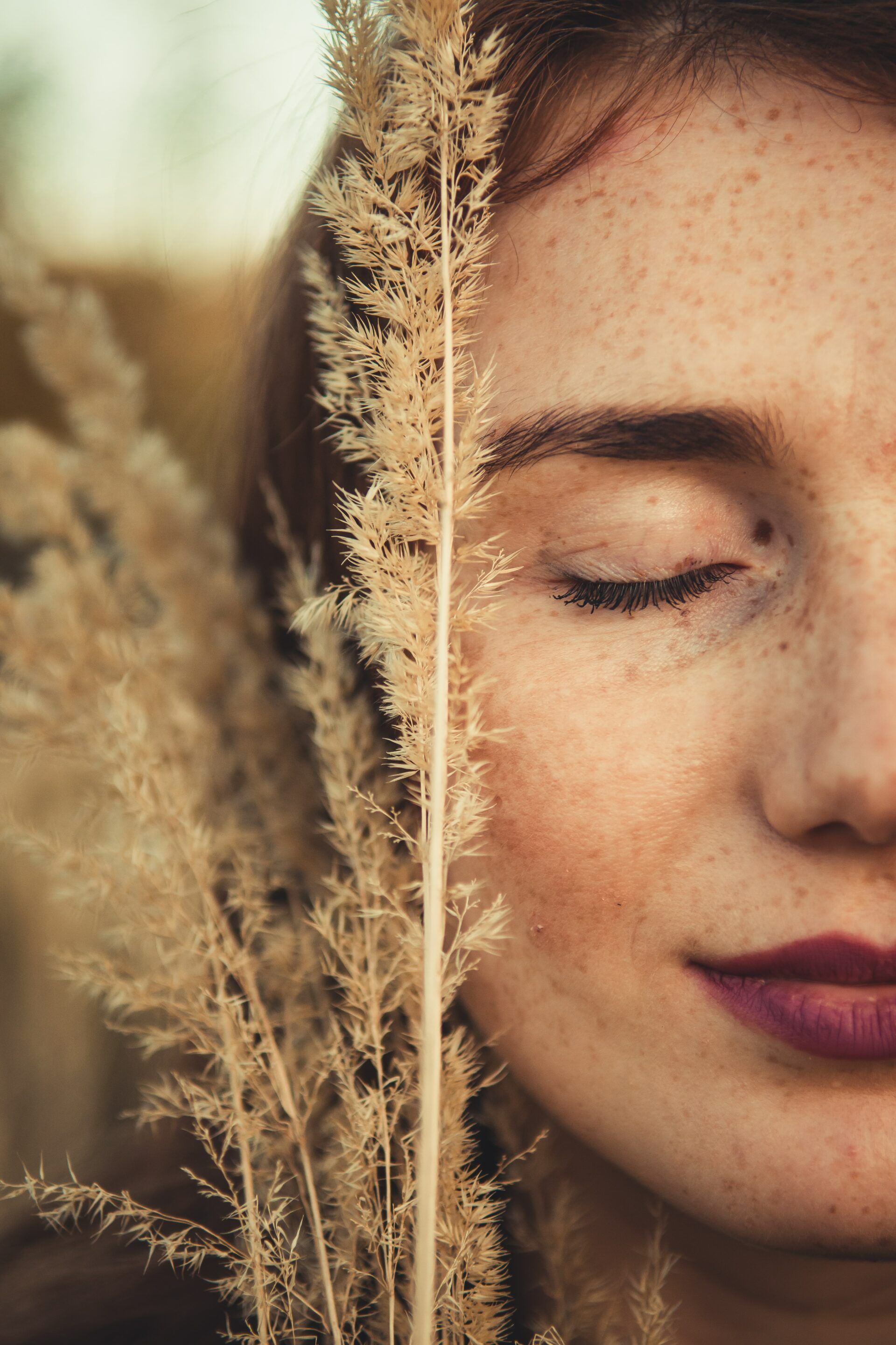 A woman with her eyes closed is holding a plant in front of her face.