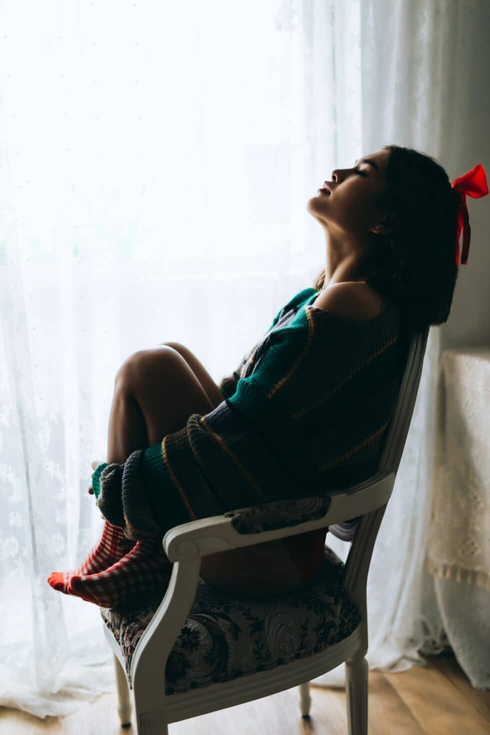 A woman is sitting in a chair in front of a window.