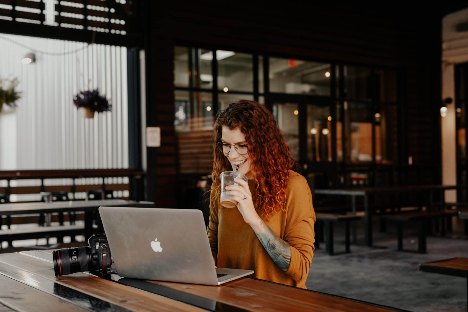 A woman is sitting at a table with a laptop and drinking a beer.