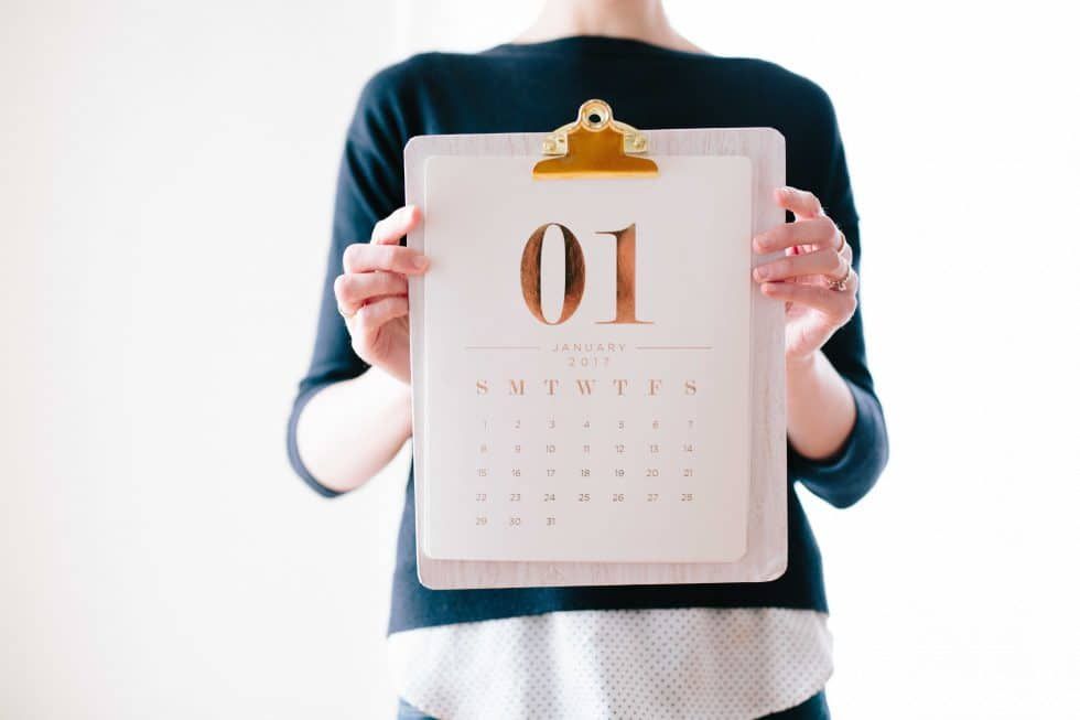 A woman is holding a clipboard with a calendar on it.