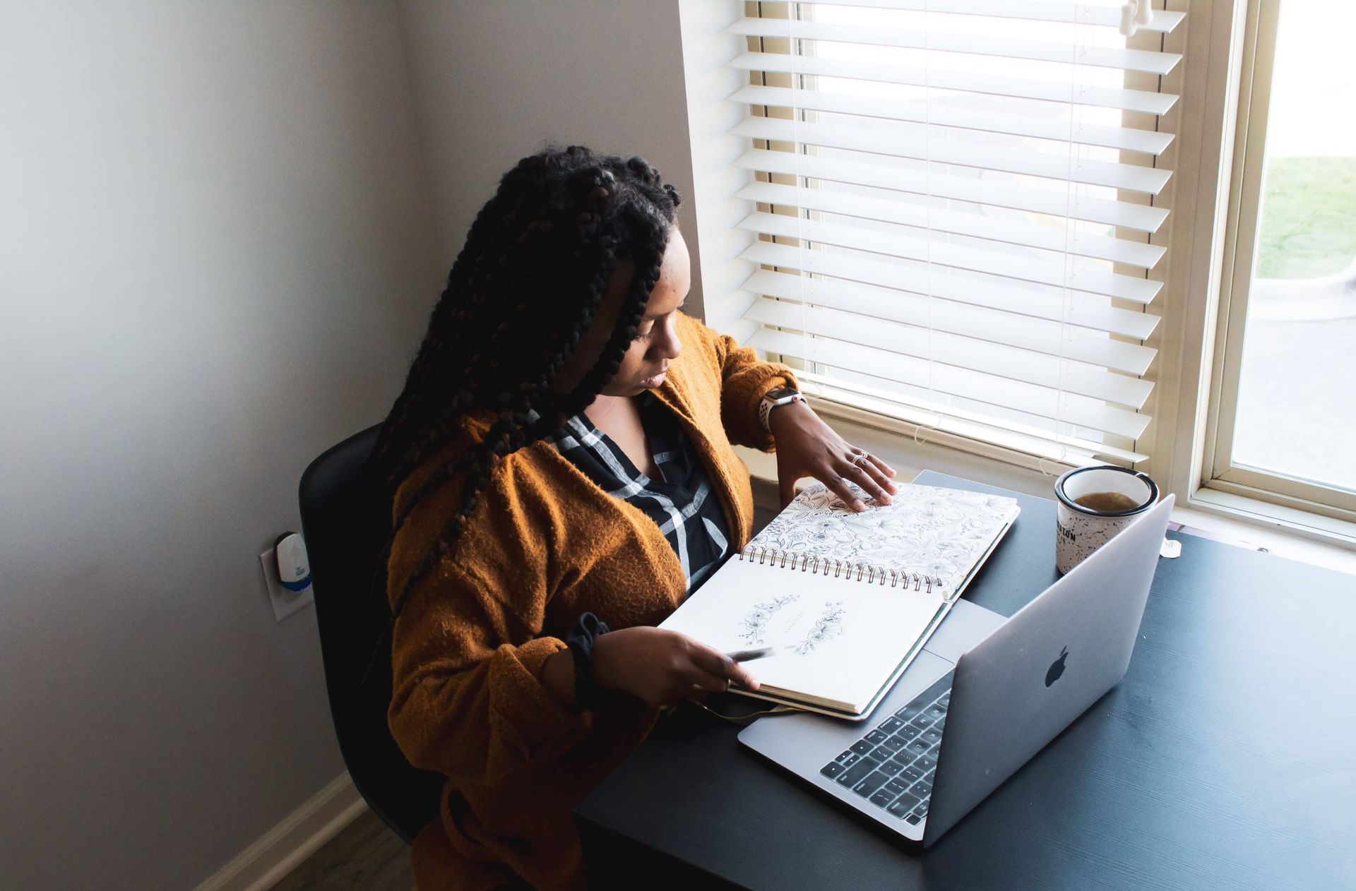 A woman is sitting at a desk with a laptop and a notebook.