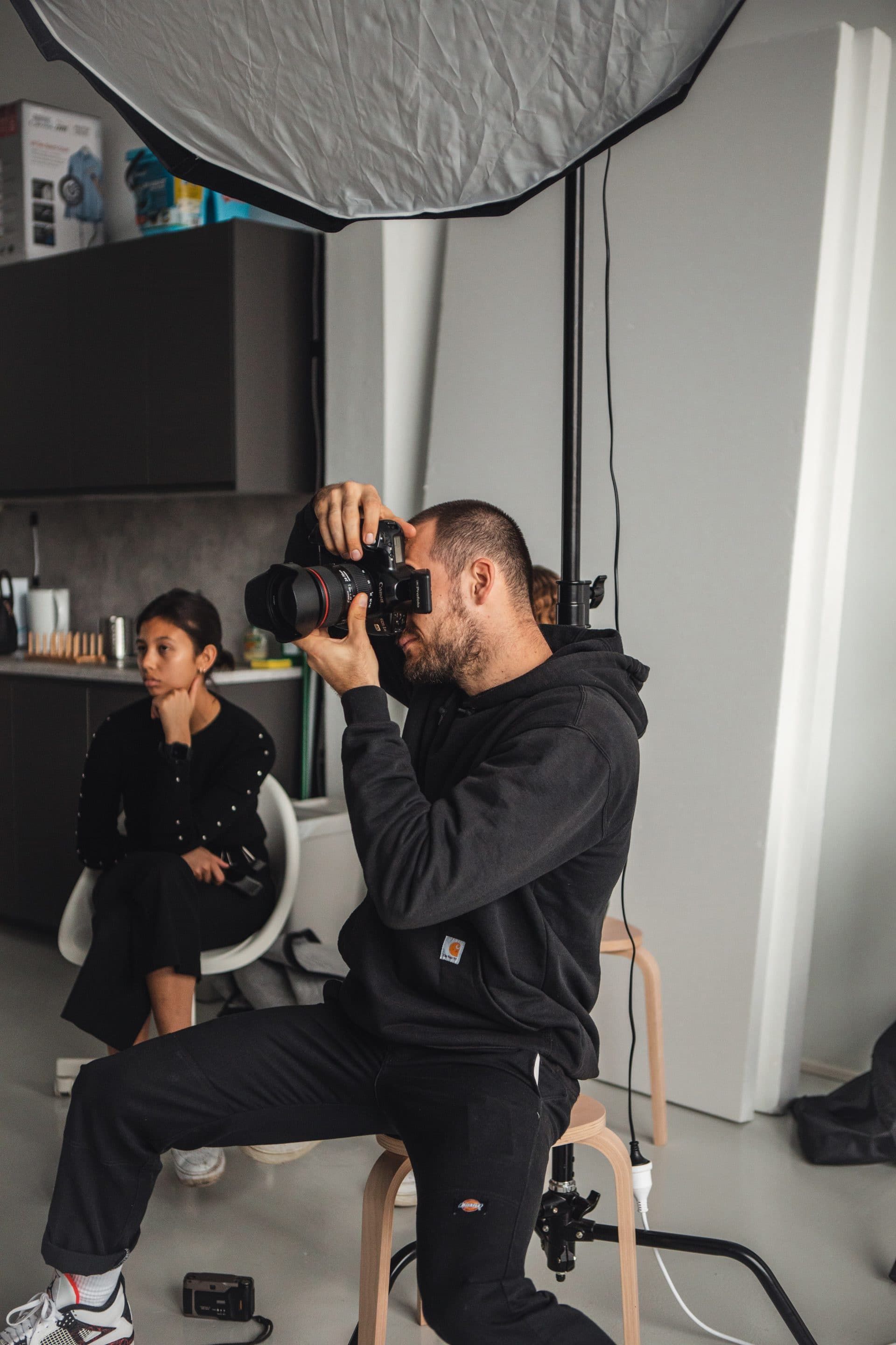 A man is sitting on a stool taking a picture of a woman with a camera.