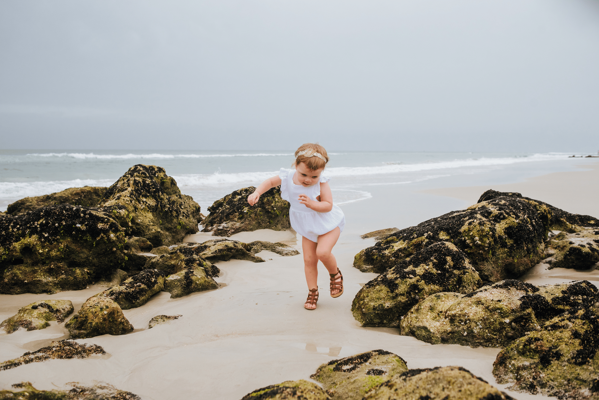 A little girl is running on a rocky beach.