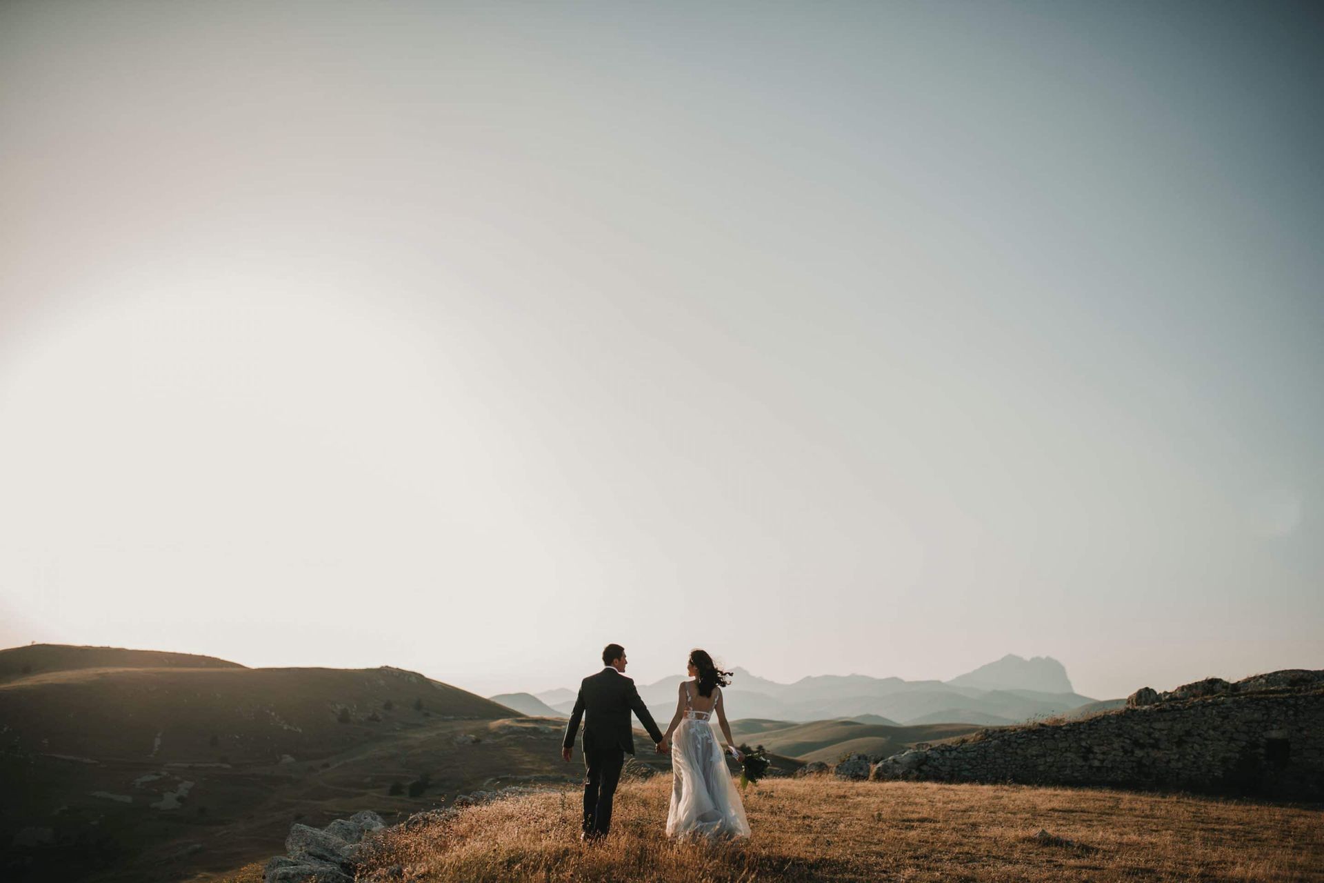 A bride and groom are walking down a hill holding hands.