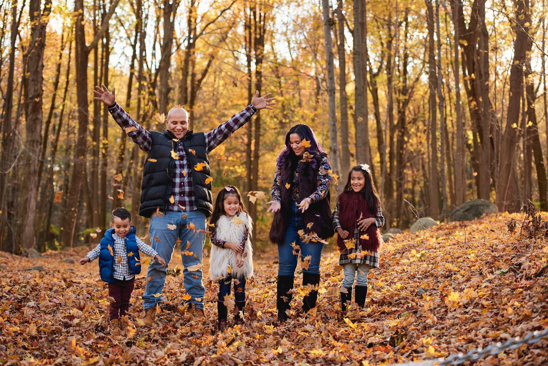 A family is throwing leaves in the air in the woods.