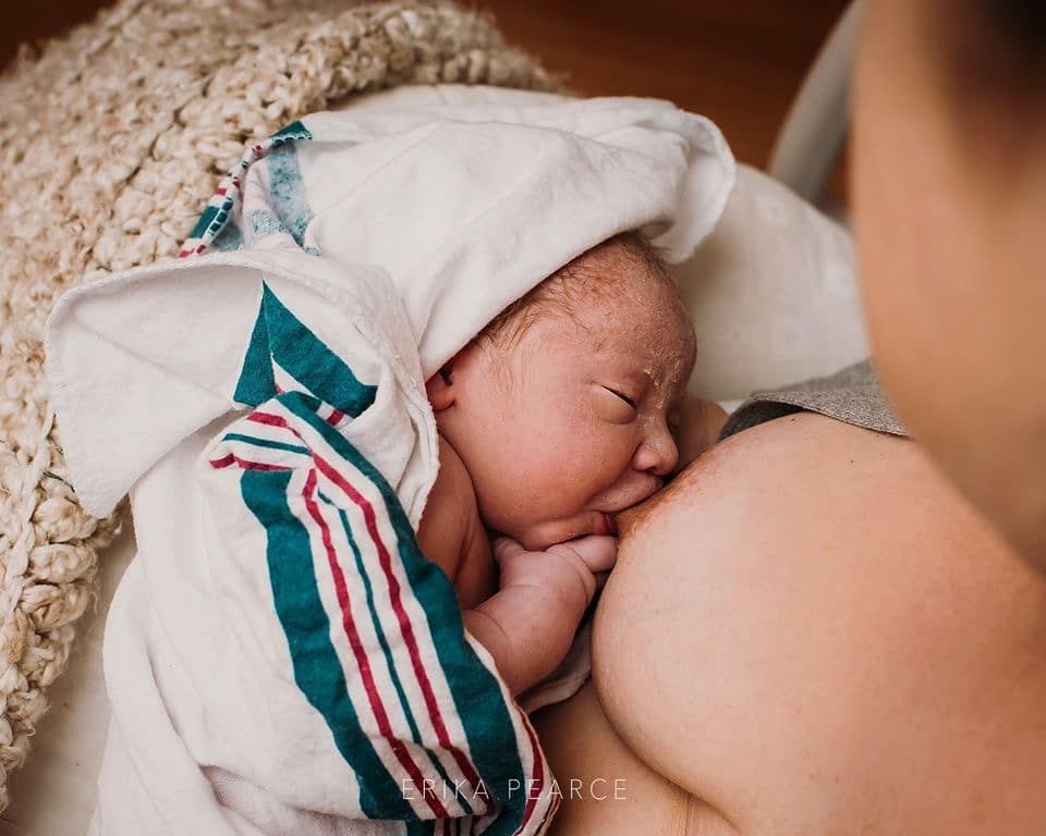 A woman is breastfeeding a newborn baby wrapped in a hospital gown.