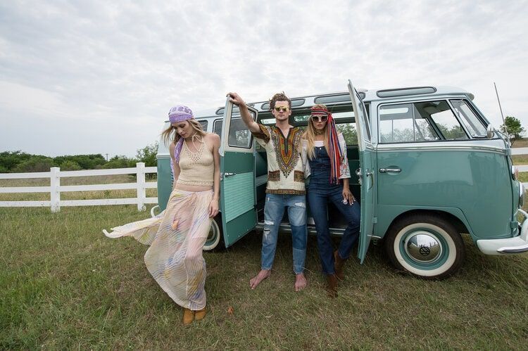 Three people are standing next to a blue van in a field.