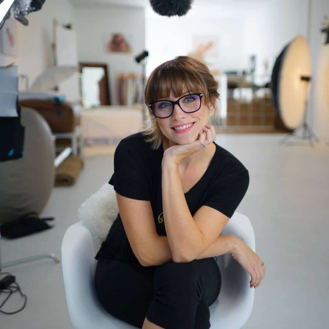 A woman wearing glasses and a black shirt is sitting in a chair.