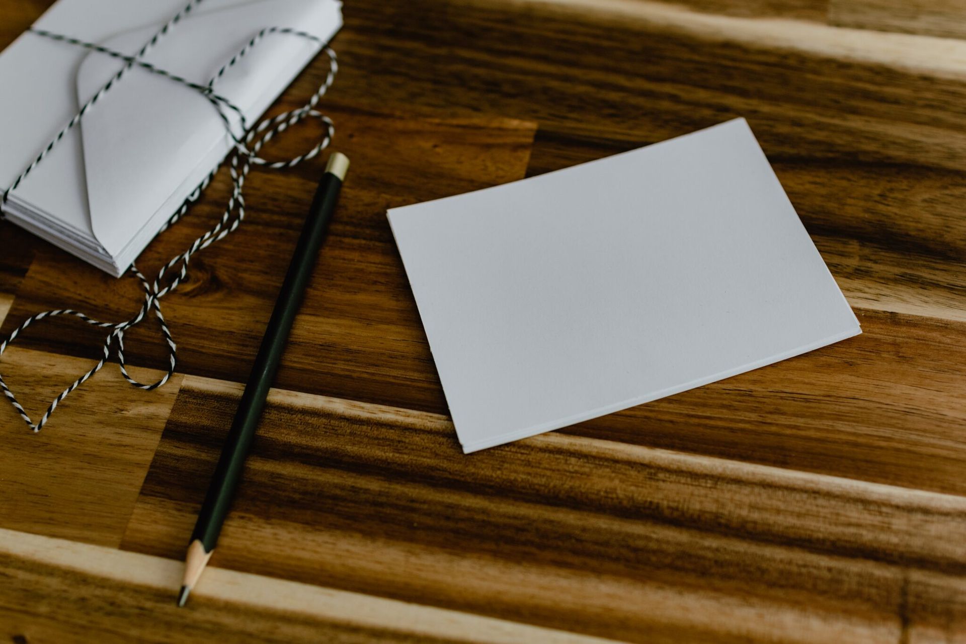 A stack of envelopes , a card and a pencil on a wooden table.