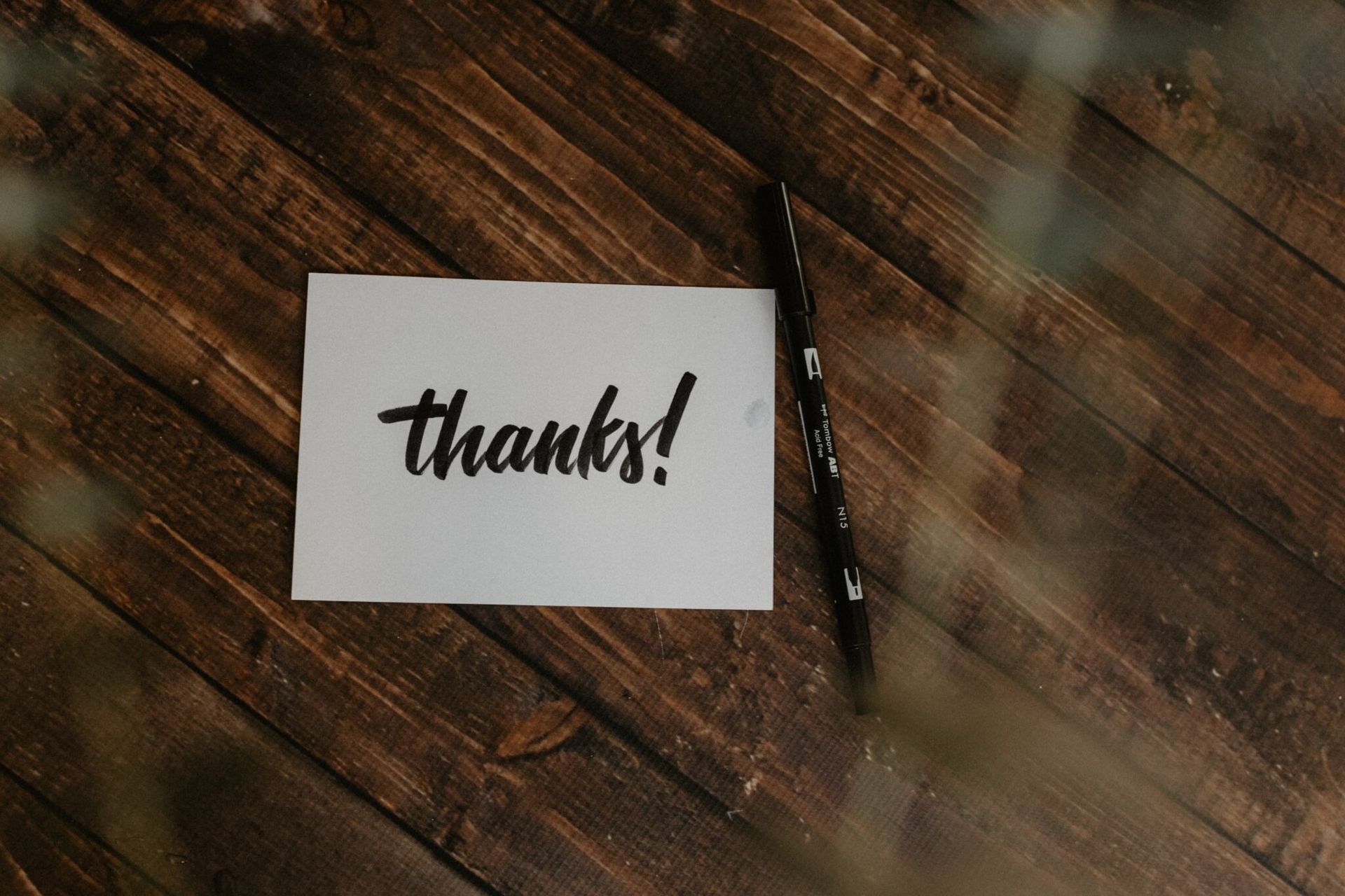 A thank you card is sitting on a wooden table next to a pen.