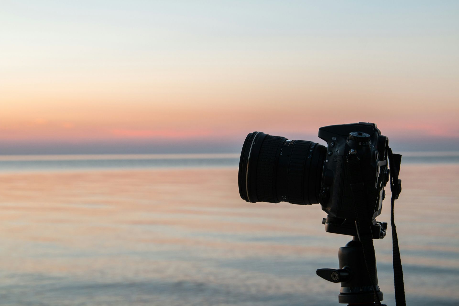 A camera is sitting on a tripod in front of the ocean at sunset.