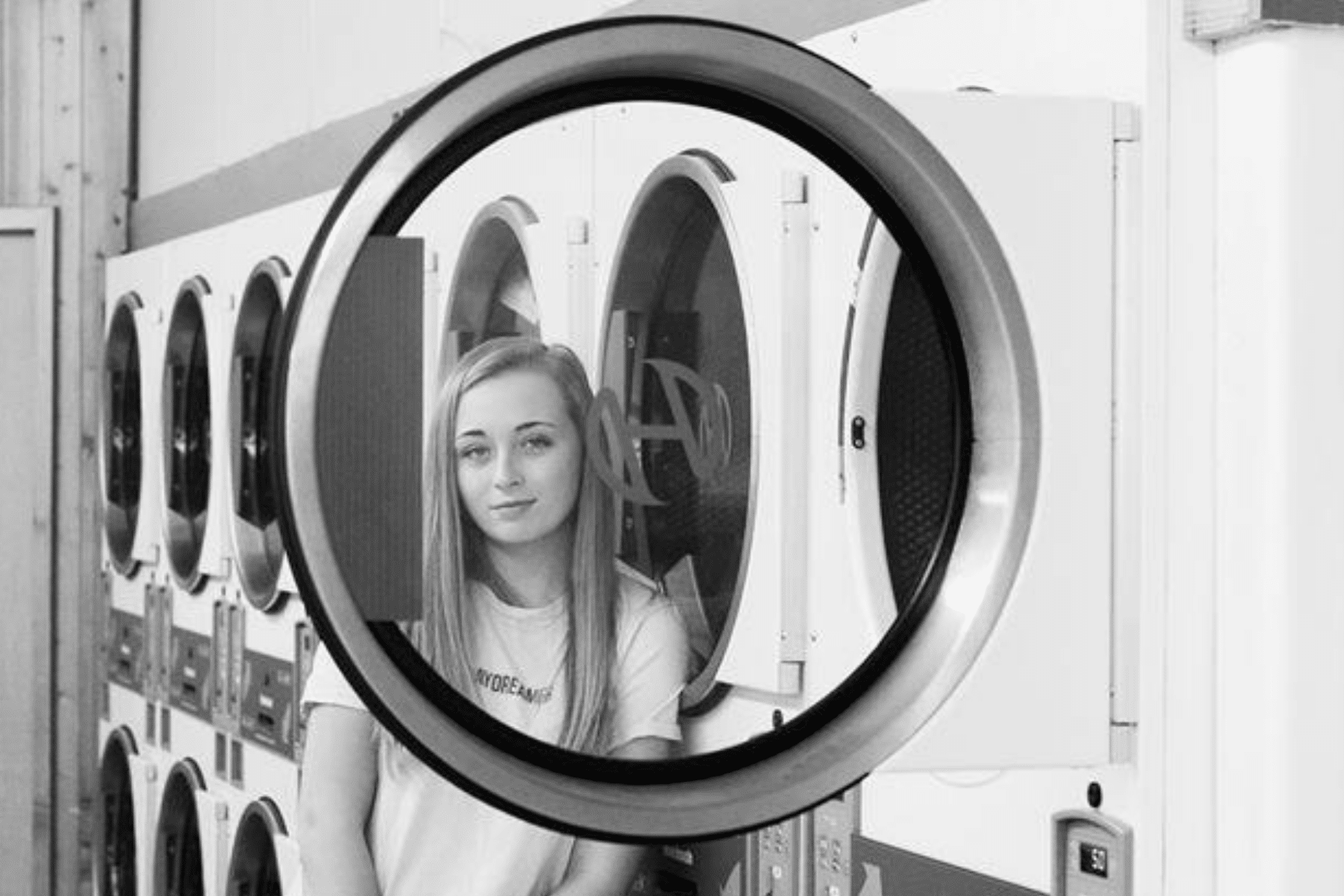 A woman is standing in front of a washing machine in a laundromat.