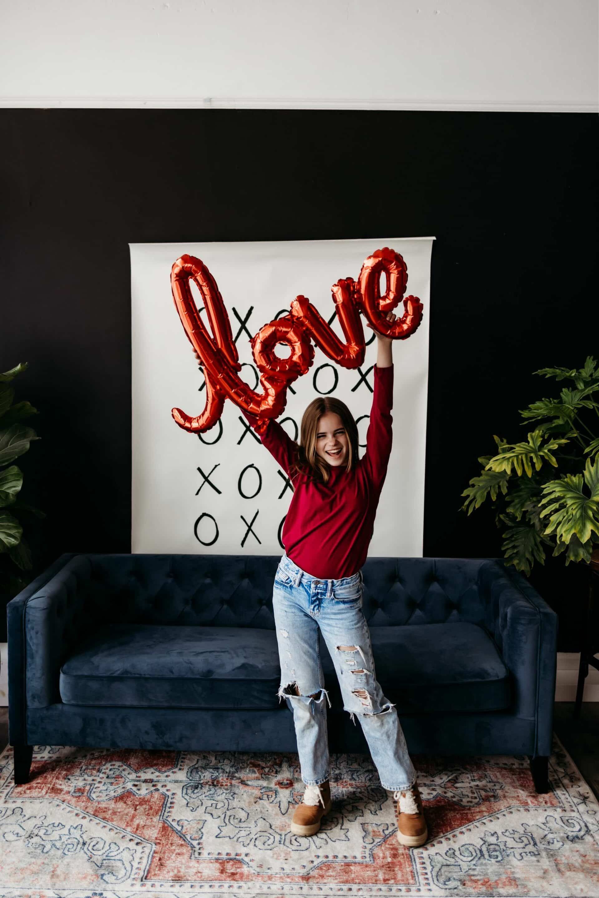 A woman is holding a red love balloon in front of a couch.