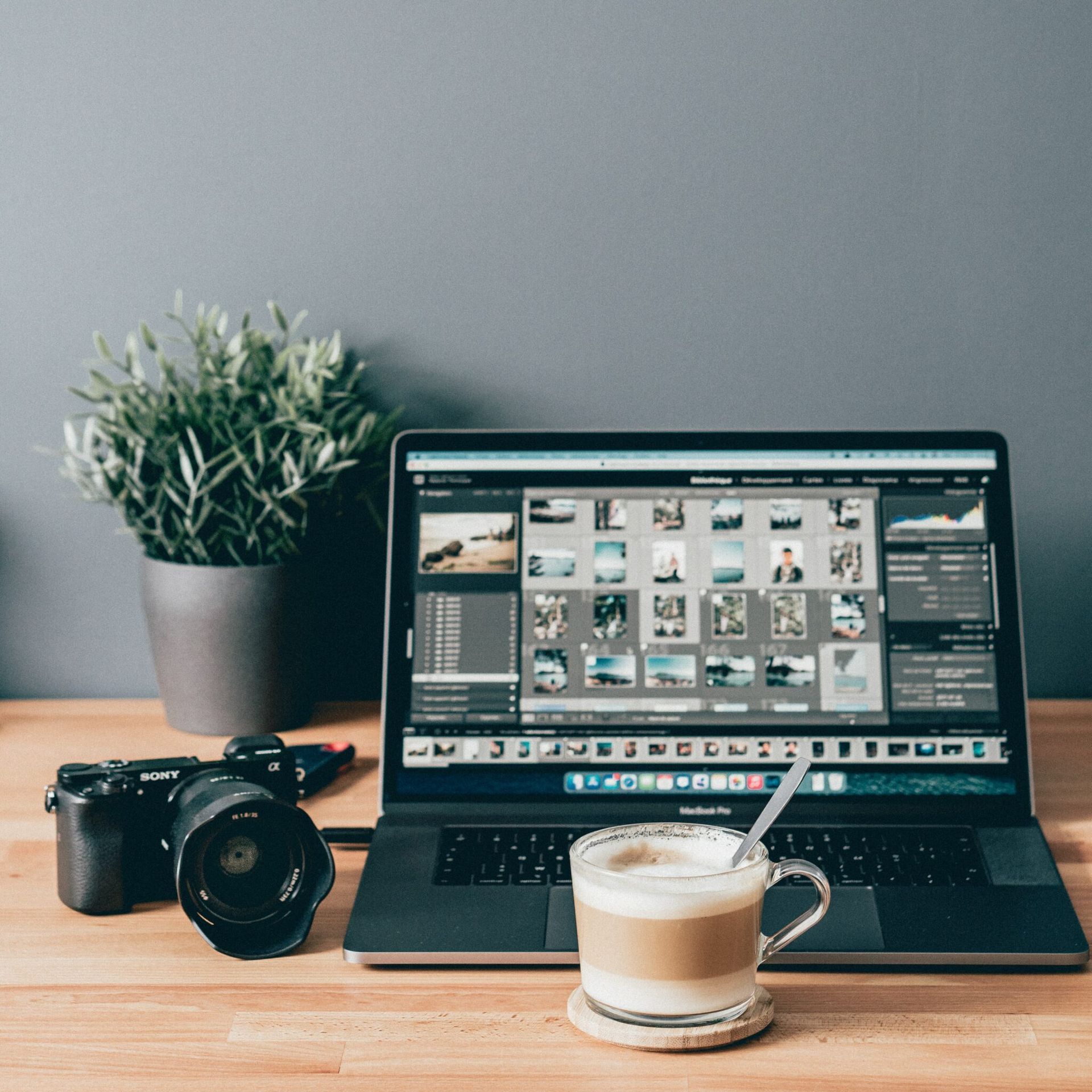 A laptop is open on a wooden desk next to a camera and a cup of coffee