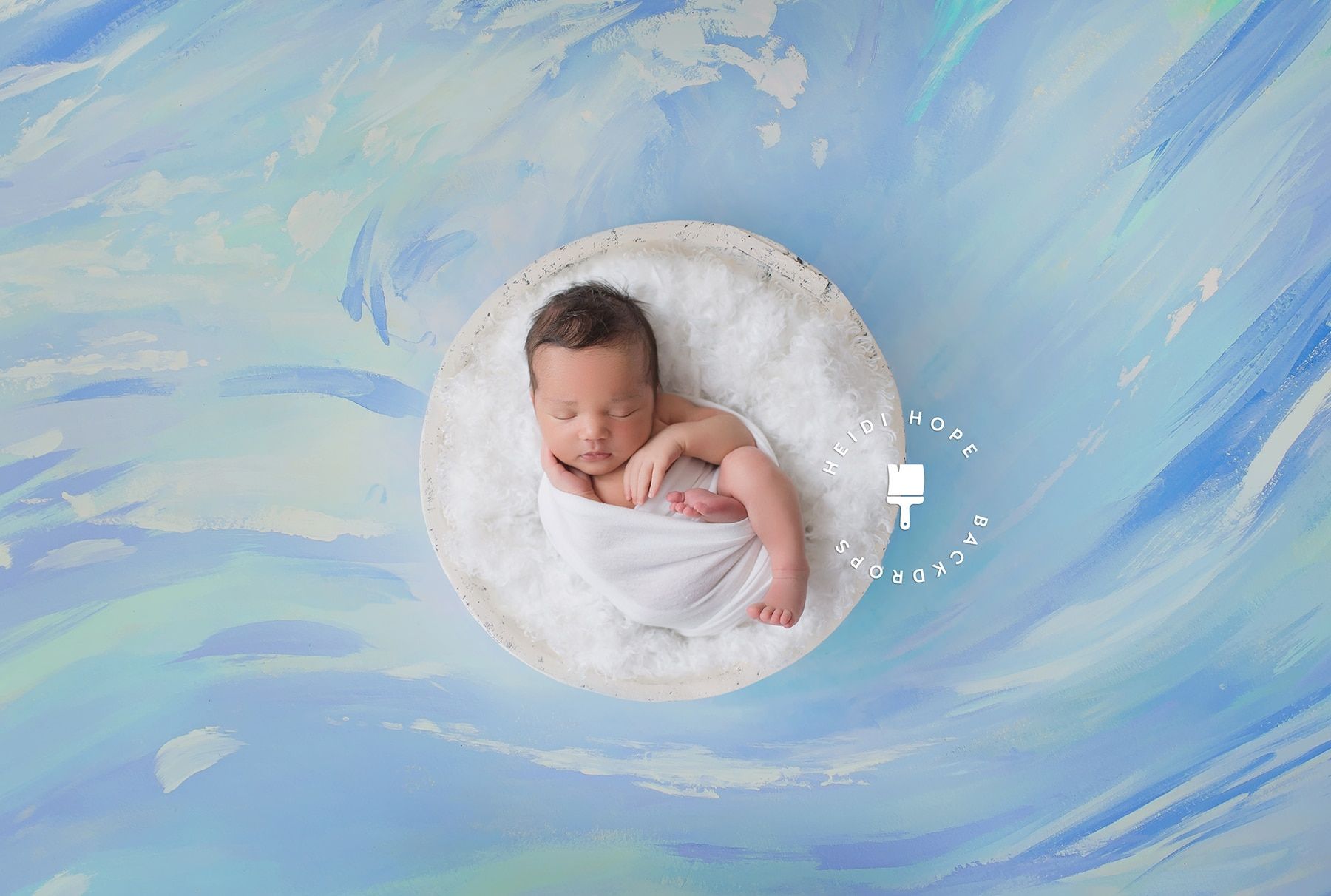 A newborn baby is sleeping in a bowl on a blue background.