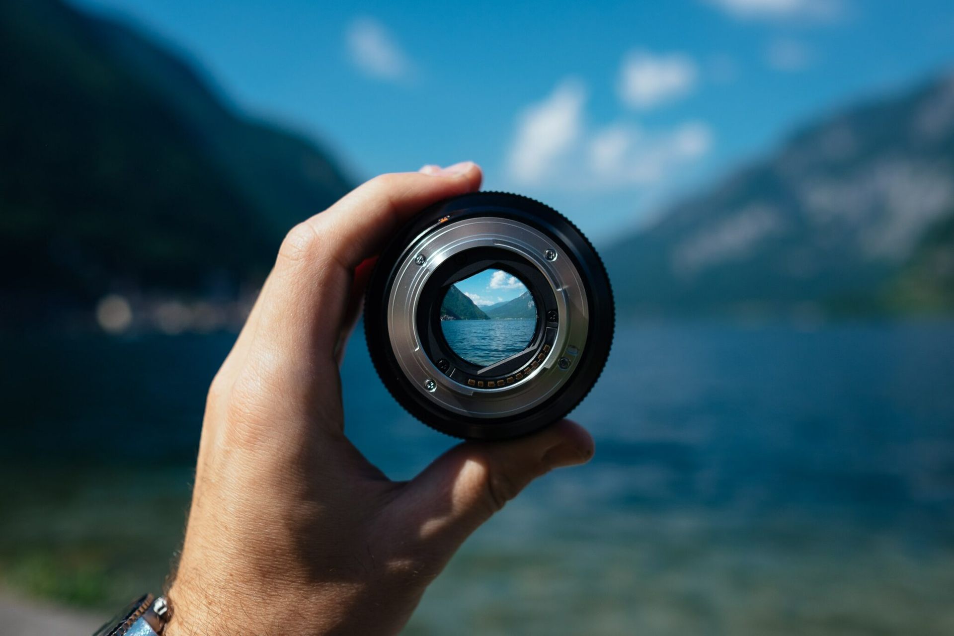 A person is holding a camera lens in front of a lake.