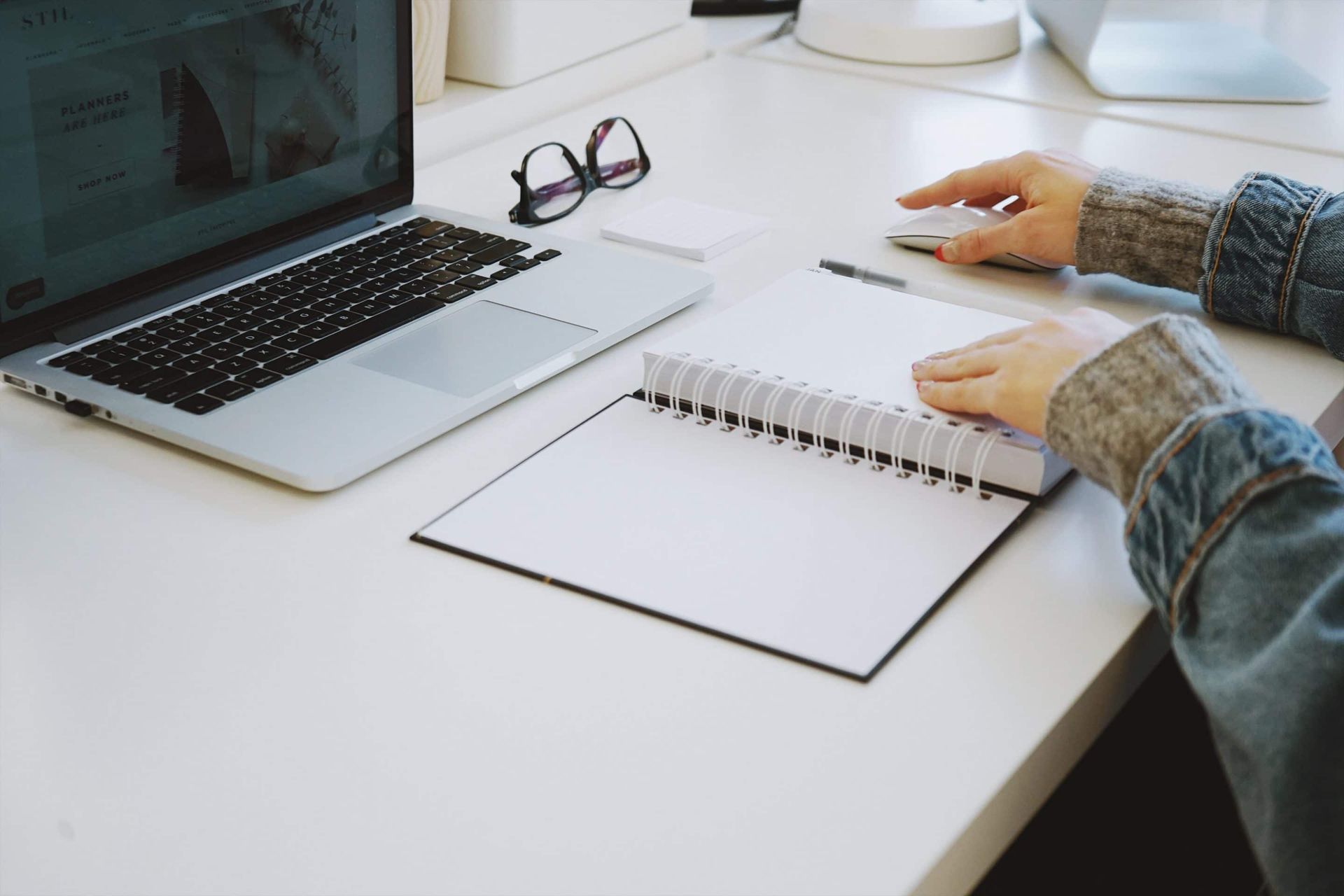 A person is sitting at a desk with a laptop and a notebook.