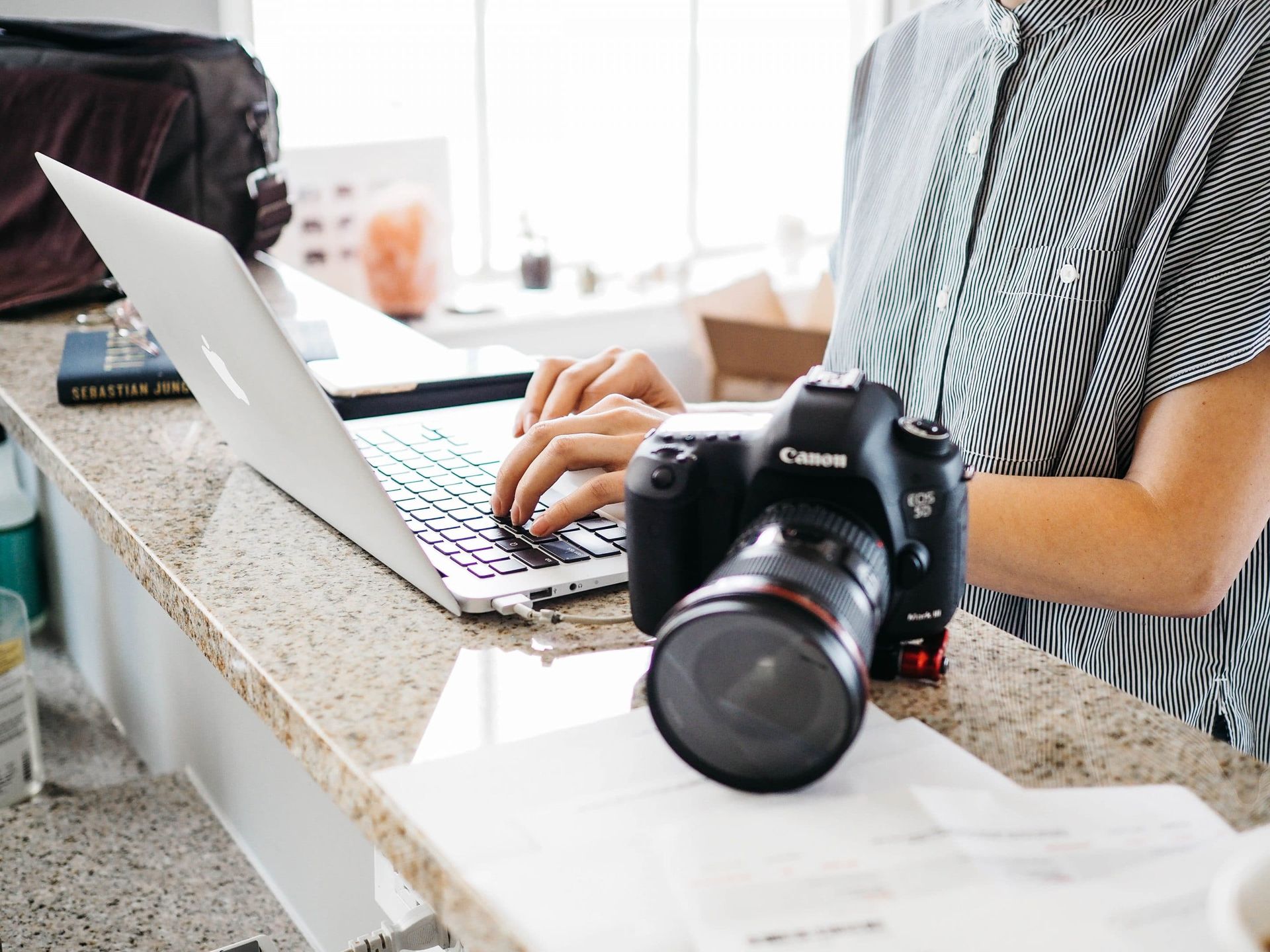 A woman is typing on a laptop next to a camera.