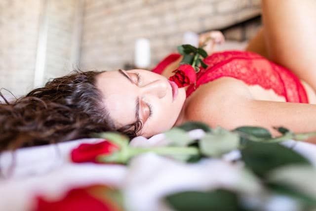 A woman in lingerie is laying on a bed with roses.